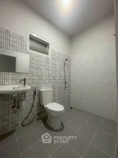 Modern minimalist bathroom with tiled walls and floor, featuring a shower and toilet.