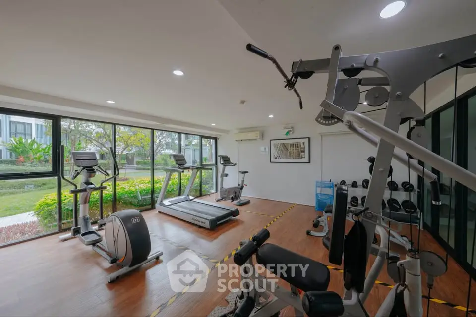 Modern gym with exercise equipment and large windows overlooking greenery.