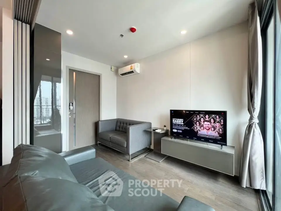 Modern living room with sleek furniture and large window offering city views.