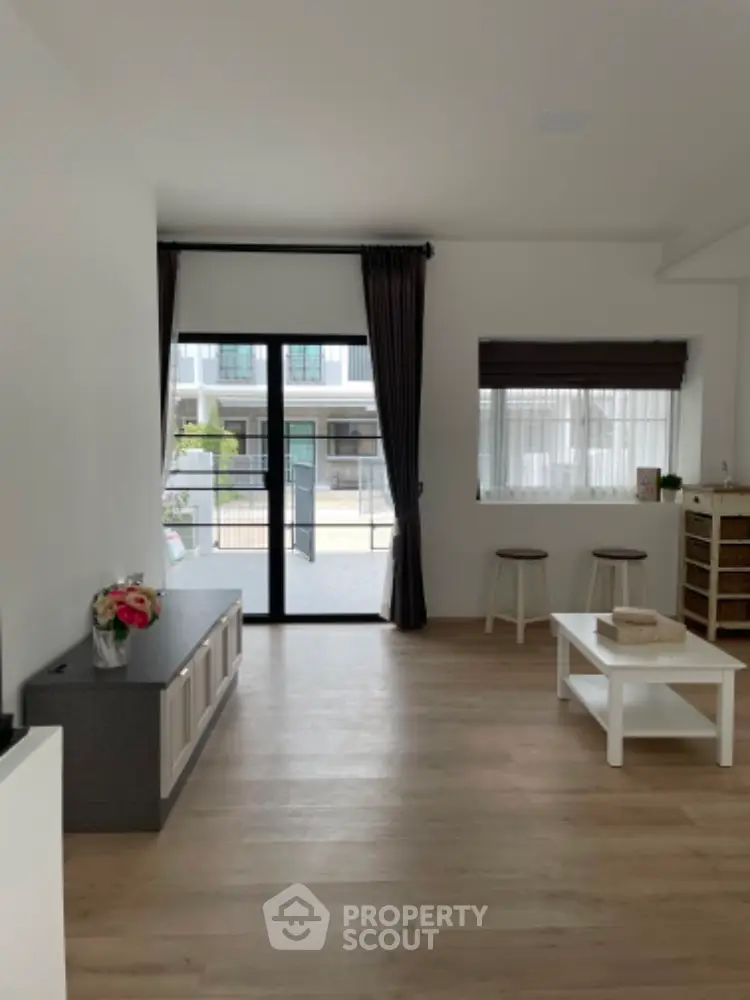 Spacious and modern living room with sleek hardwood floors, abundant natural light, and a cozy minimalist design, leading to a charming balcony.