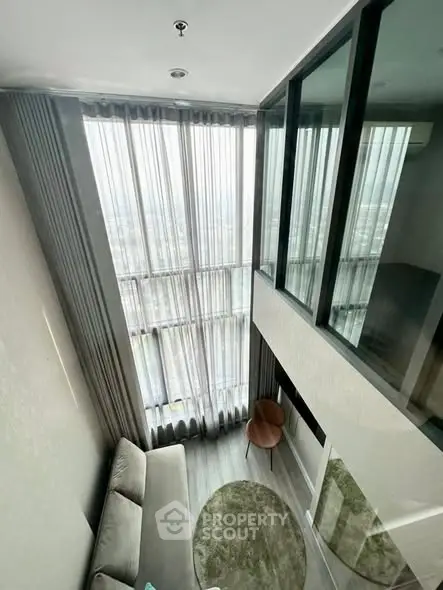 Modern high-ceiling living room with large windows and stylish decor.