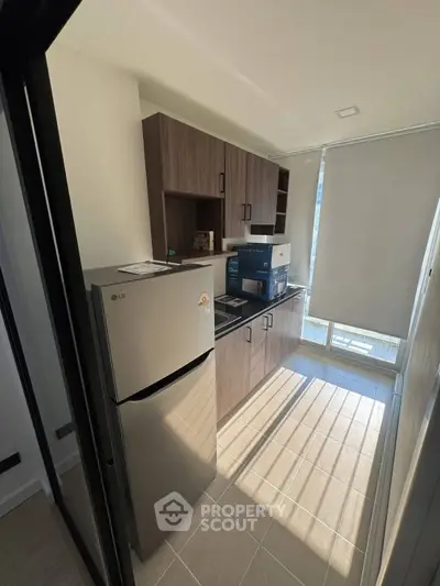 Modern kitchen with sleek cabinetry and stainless steel fridge in a sunlit apartment.