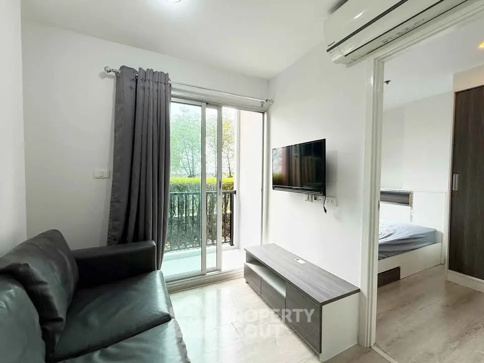 Modern living room with sleek black sofa, wall-mounted TV, and sliding glass doors to balcony.