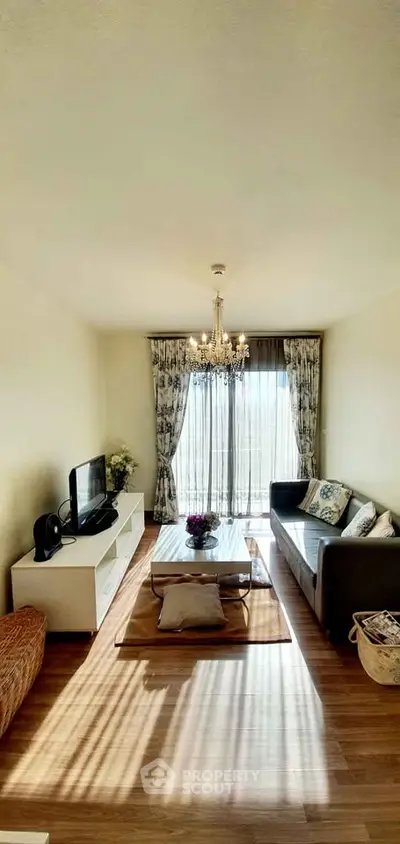 Elegant living room with chandelier, cozy seating, and natural light through large window.