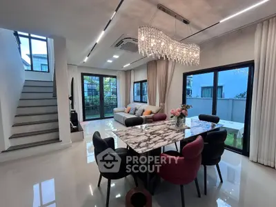 Luxurious modern living room with elegant chandelier and marble dining table, featuring large windows and garden view.