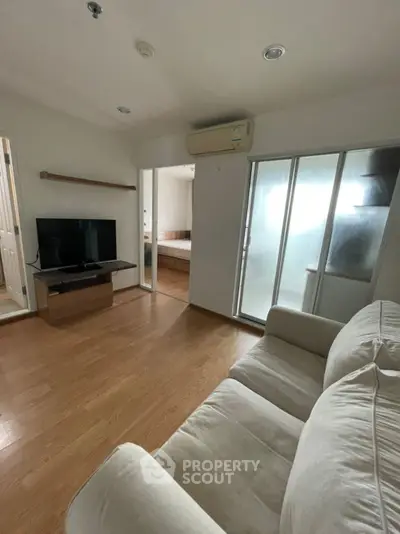Cozy living room with modern TV setup and comfortable sofa, adjacent to a bedroom.