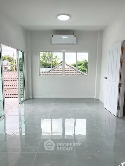 Bright room with large windows and balcony access, featuring sleek tiled flooring and air conditioning.