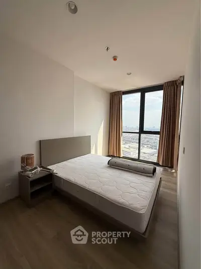 Modern bedroom with large window offering stunning city view, featuring minimalist decor and natural light.