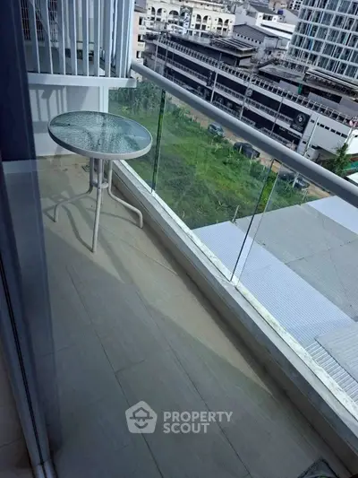 Modern balcony with glass railing offering city views and a small round table.