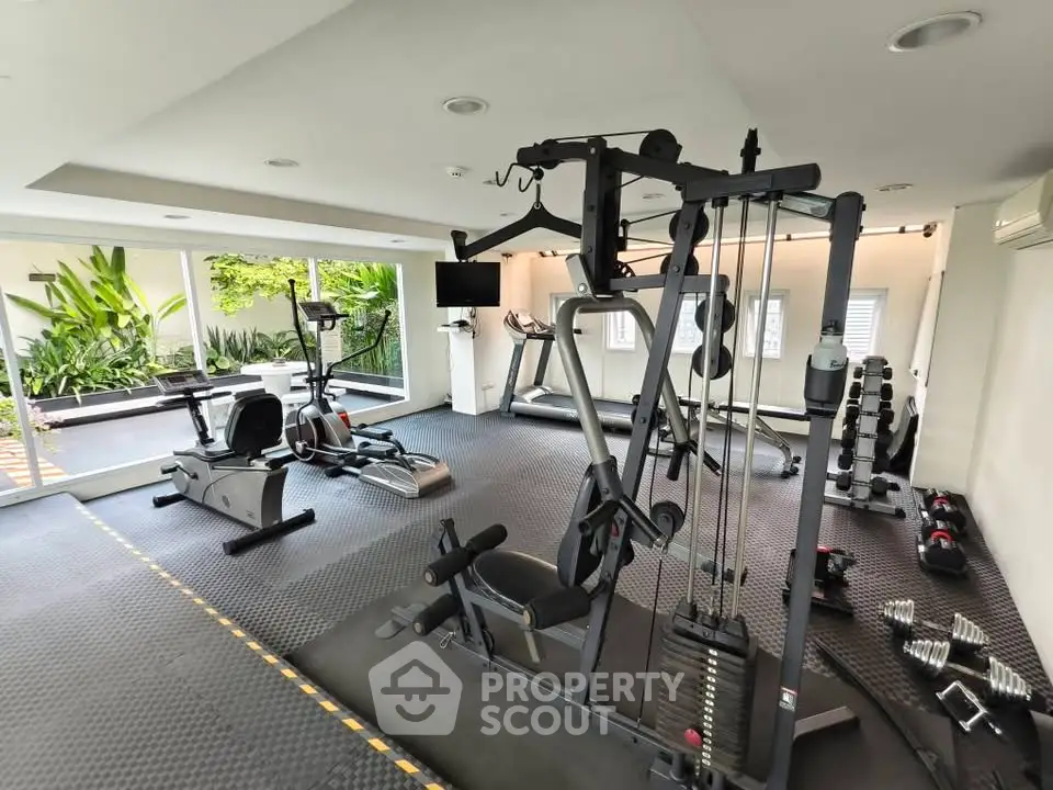 Modern gym with state-of-the-art equipment and lush garden view, perfect for fitness enthusiasts.