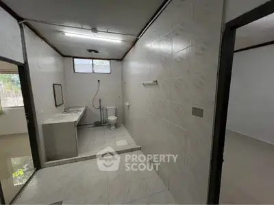 Spacious bathroom with tiled walls and floor, featuring a large sink and toilet.