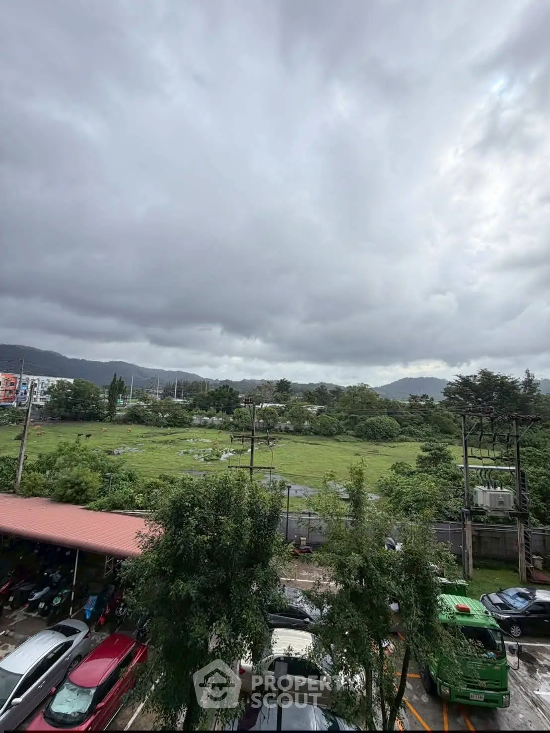 Scenic view of lush green landscape with parked cars and cloudy sky, ideal for real estate development.