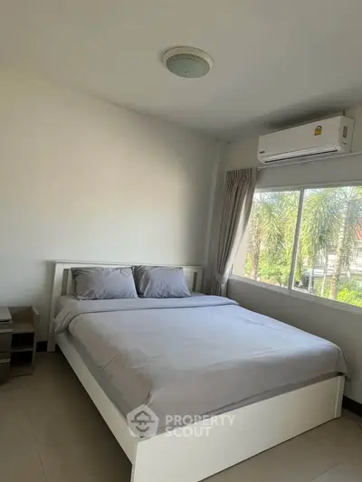 Cozy bedroom with large window and air conditioning, offering a serene view of lush greenery.
