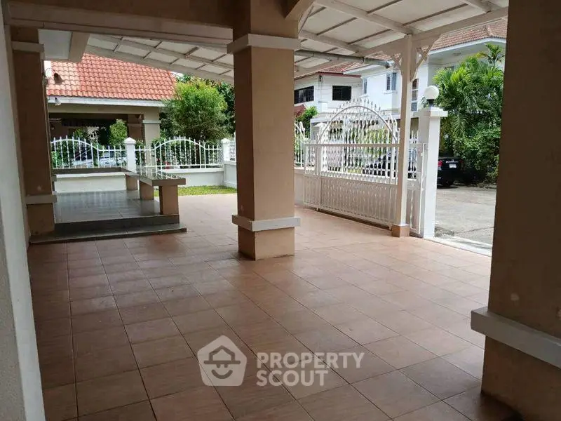 Spacious covered parking area in a residential property with tiled flooring and gated entrance.