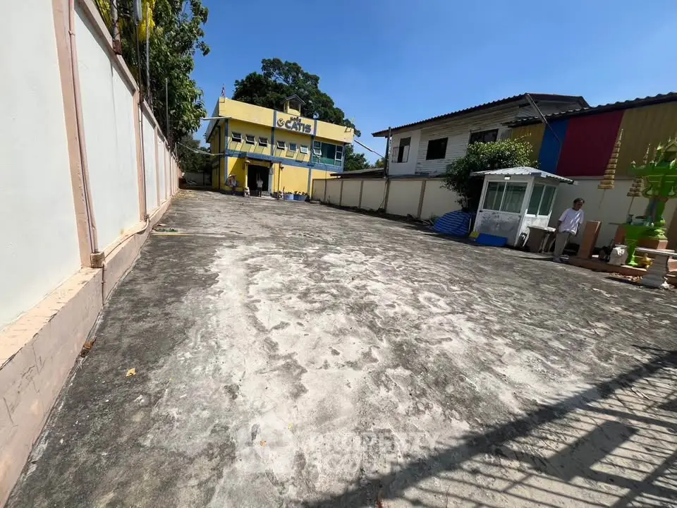 Spacious outdoor area with a paved surface and a yellow building in the background, ideal for commercial use.