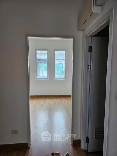 Bright room with wooden flooring and large windows offering natural light.