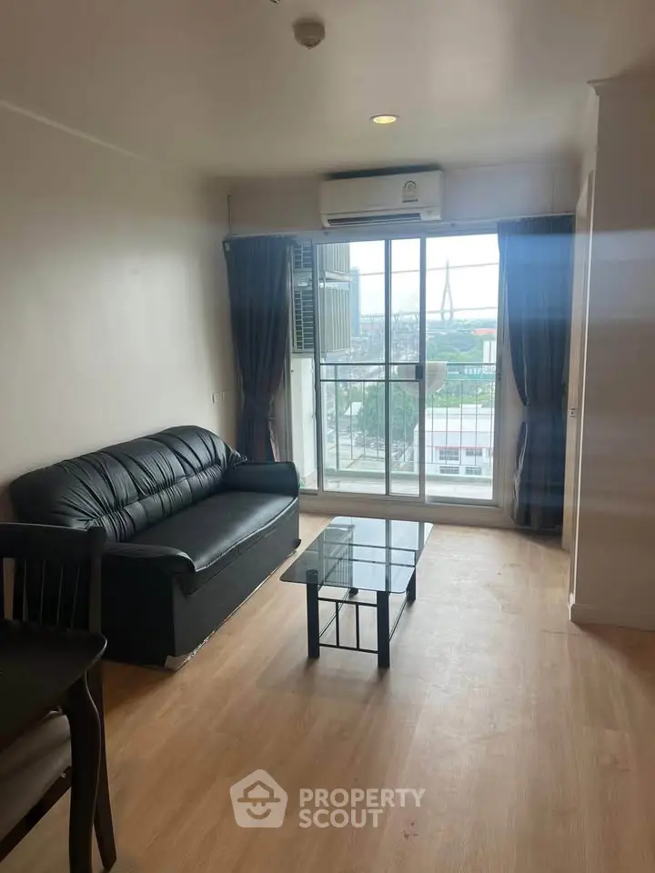 Modern living room with black leather sofa and glass coffee table, featuring a large window with city view.
