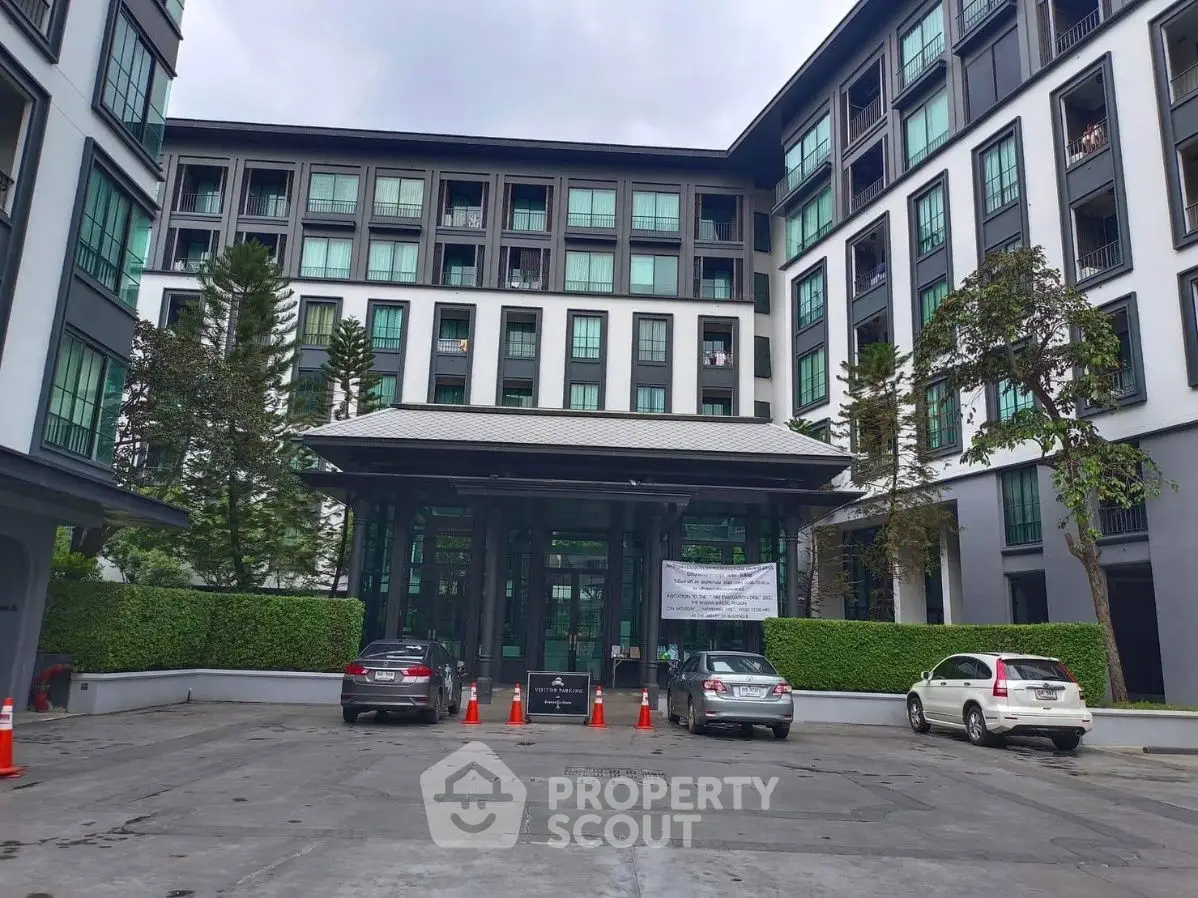 Modern residential building entrance with parked cars and lush greenery