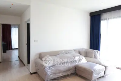 Spacious living room with modern furniture wrapped for protection, featuring large windows and natural light.