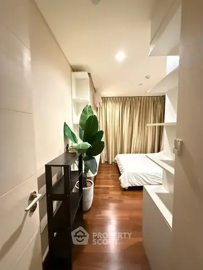 Cozy bedroom with wooden flooring and elegant decor, featuring a large plant and soft lighting for a serene ambiance.