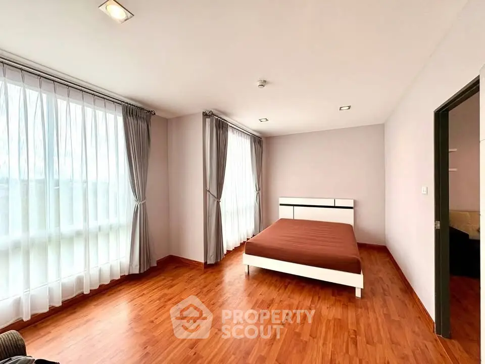 Spacious bedroom with large windows and wooden flooring in modern apartment