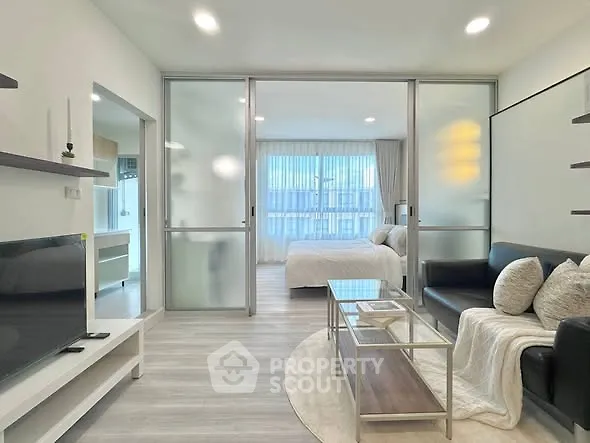 Modern open-plan living room with sleek glass partitions and cozy bedroom view.