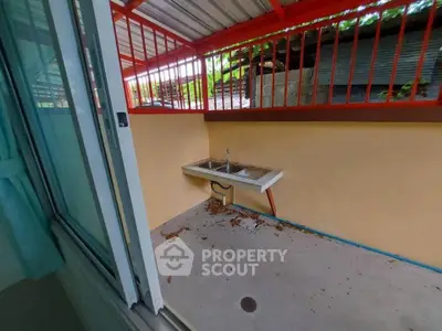 Outdoor kitchen area with metal sink and open layout, featuring a covered roof and red railing.