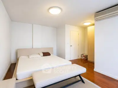Spacious bedroom with modern design and wooden flooring, featuring a comfortable bed and air conditioning.