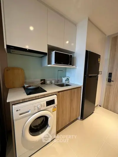 Modern compact kitchen with appliances including washing machine, microwave, and fridge in stylish apartment.