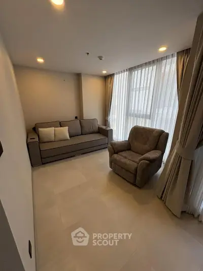 Cozy living room with modern sofa and armchair, natural light from large windows