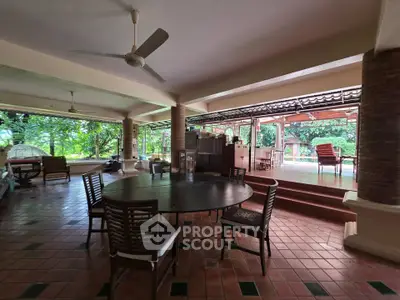 Spacious open-air living area with elegant wooden furniture and lush garden view.