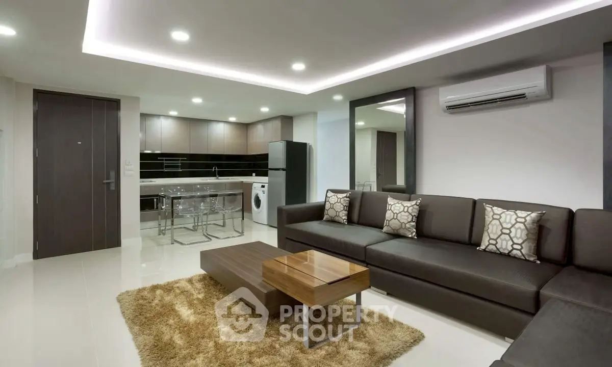 Modern living room with open kitchen, sleek furniture, and ambient lighting.