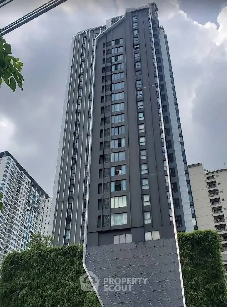Modern high-rise building with unique architectural design and lush greenery at the base.