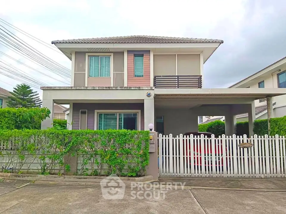 Charming two-story house with a white picket fence and lush greenery in a serene neighborhood.