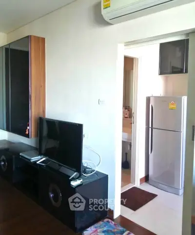 Modern living room with sleek TV unit and visible kitchen appliances