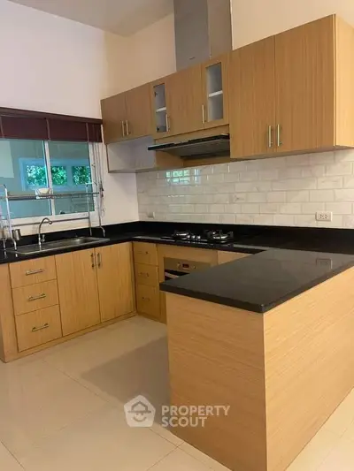 Modern kitchen with sleek wooden cabinetry, black countertops, and a gas stove, perfect for culinary enthusiasts.