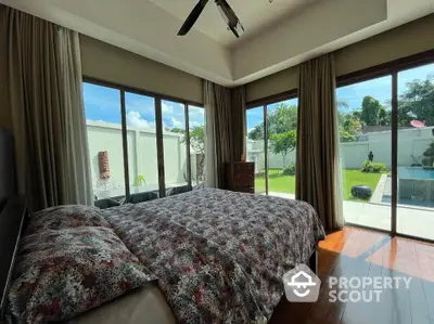 Spacious bedroom with garden and pool view, featuring large windows and elegant decor.