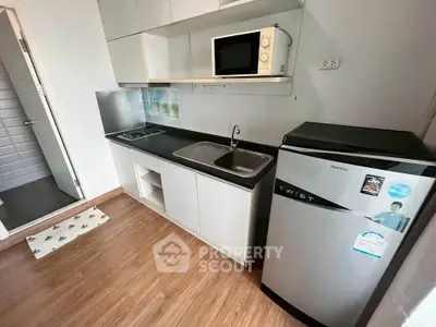 Modern compact kitchen with sleek appliances and wooden flooring in a cozy apartment.