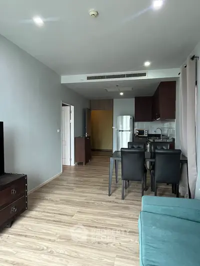 Modern open-plan living room with dining area and kitchen, featuring sleek furniture and wooden flooring.