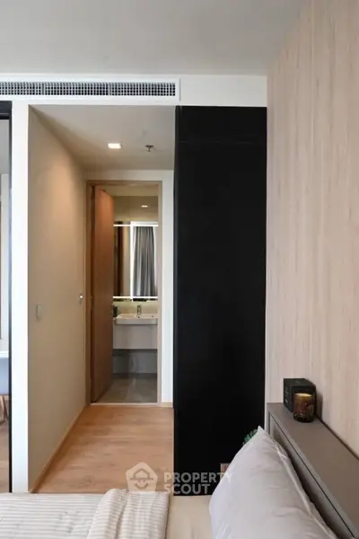 Modern bedroom with view into a sleek bathroom, featuring contemporary design and neutral tones.