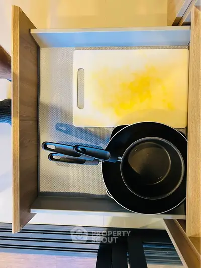 Modern kitchen drawer with cutting board and frying pans in stylish apartment.