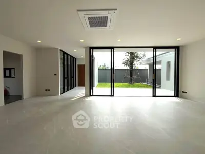 Spacious modern living room with large glass doors opening to a lush garden view.