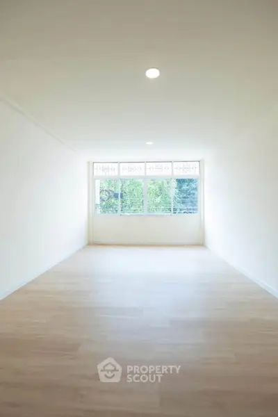 Spacious empty room with large window and wooden flooring, ideal for customization.