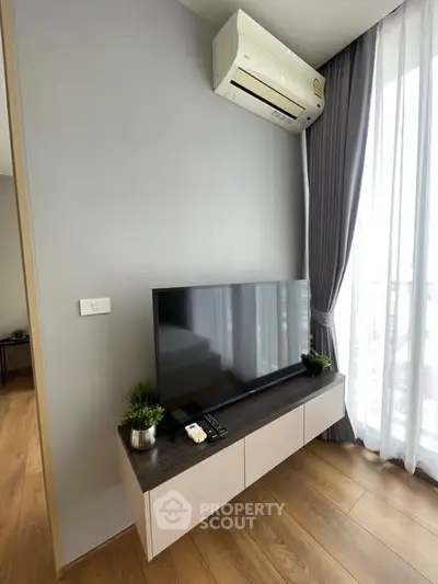 Modern living room with sleek TV setup and air conditioning, featuring elegant curtains and wooden flooring.