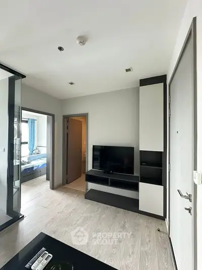 Modern living room with sleek TV unit and view into bedroom, showcasing contemporary apartment design.