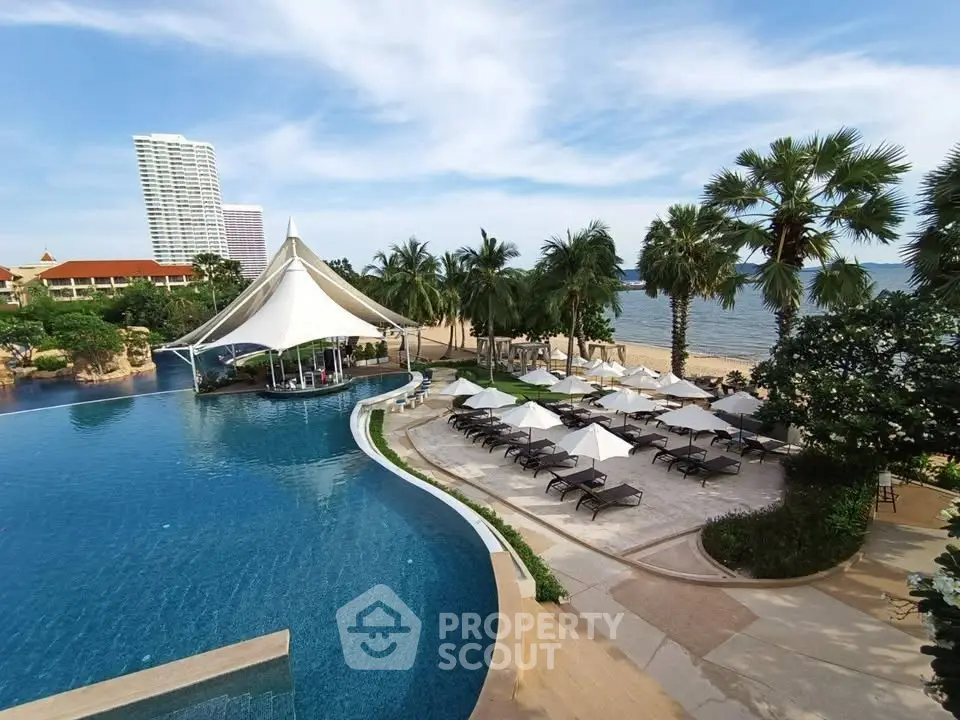 Luxurious beachfront pool area with palm trees and sun loungers, perfect for relaxation and leisure.