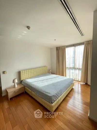 Spacious bedroom with wooden flooring and large window for natural light.