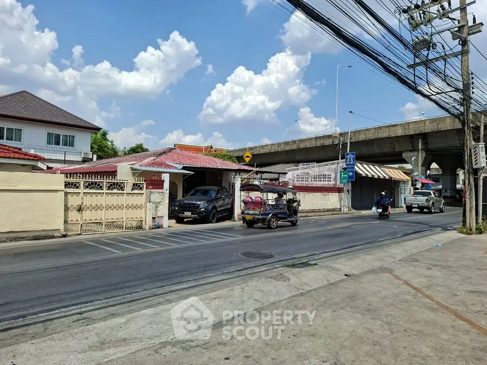 Charming urban street view with residential houses and a tuk-tuk under a clear blue sky.