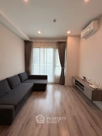 Modern living room with sleek sofa and air conditioning, featuring large window and wooden flooring.