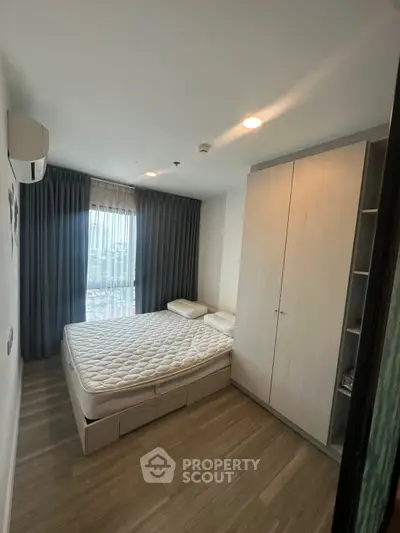 Modern bedroom with large window and sleek wardrobe in a high-rise apartment.
